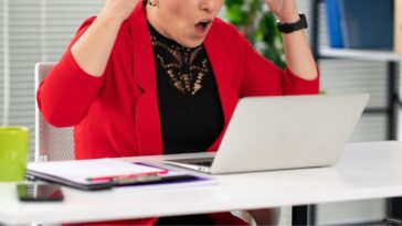 Portrait of a young, screaming businesswoman with her hands flailing around her head, yelling at a computer.