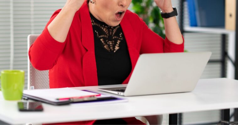 Portrait of a young, screaming businesswoman with her hands flailing around her head, yelling at a computer.
