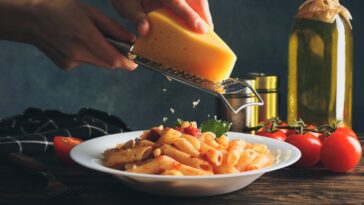 person grating cheese onto pasta