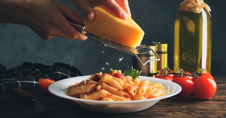 person grating cheese onto pasta