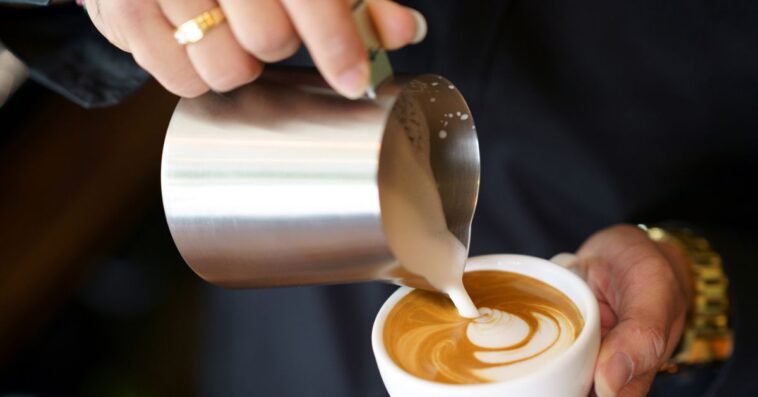 Barista hands pouring milk foam into of espresso resulting a pattern design on the surface of latte, Pouring Latte Art.