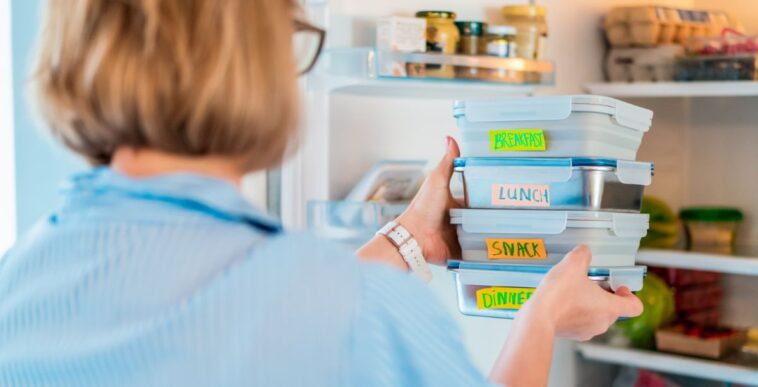 Back view shot of a woman taking or putting lunch boxes cooked in advance, ready to be served into fridge. Containers with eco healthy food. Pre-cooking concept.