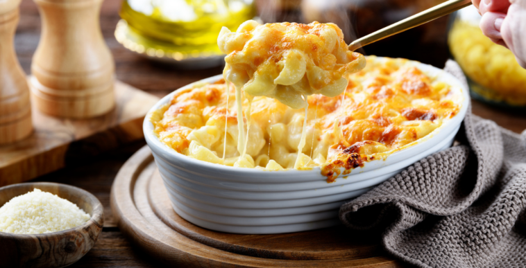 A spoon pulling out a serving of macaroni and cheese from a bowl.