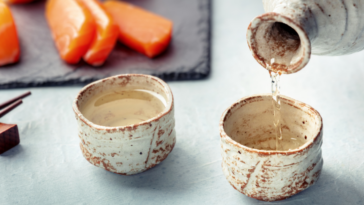 sake being poured into traditional ochoko with salmon in the background