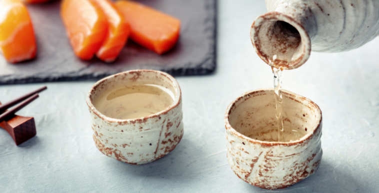 sake being poured into traditional ochoko with salmon in the background