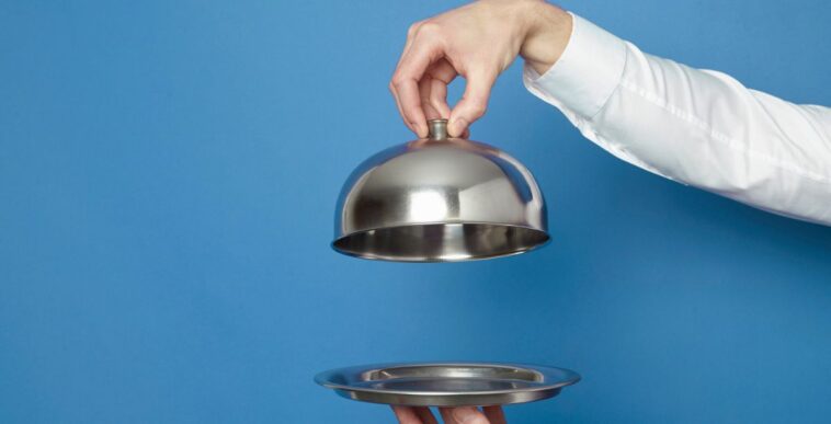 Man holding silver tray and lid against blue and green background.
