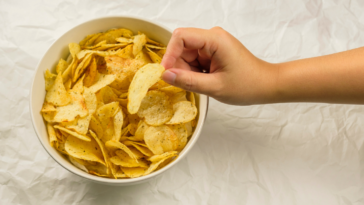 A child's hand taking a potato chip from a bowl.