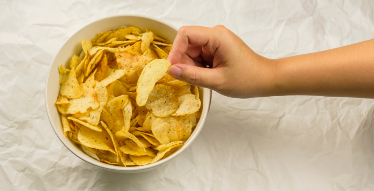 A child's hand taking a potato chip from a bowl.