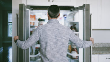 A man looking into an open refrigerator.