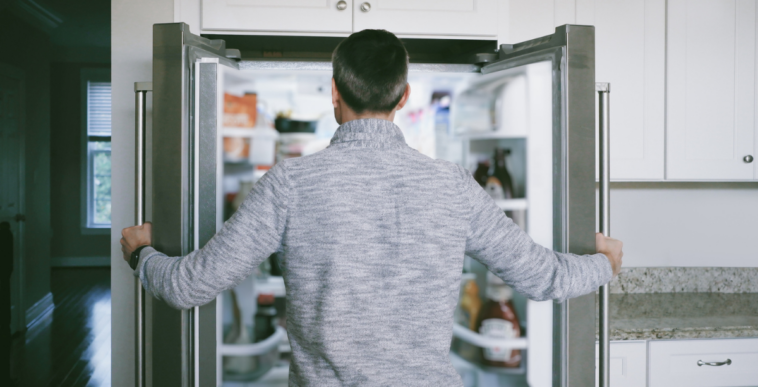 A man looking into an open refrigerator.