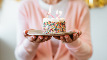 A woman holding a small birthday cake with a candle in it.