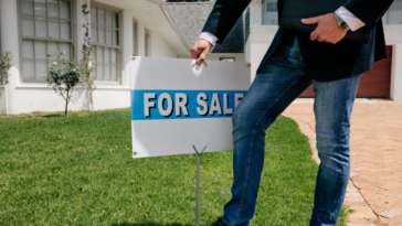 person putting "for sale" sign in front of house