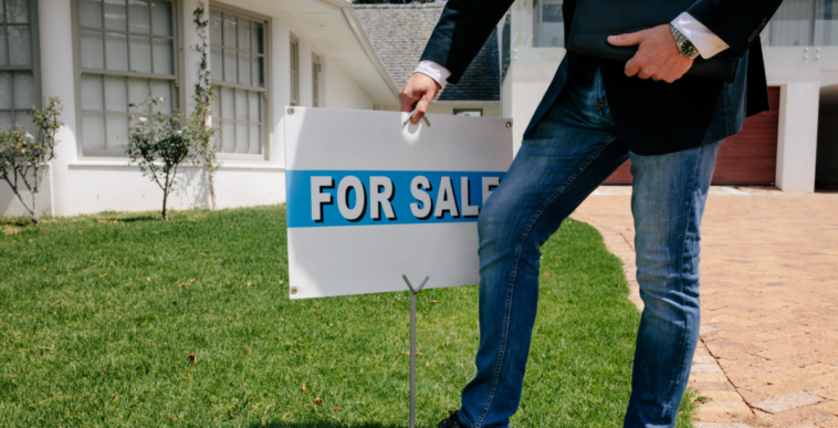 person putting "for sale" sign in front of house