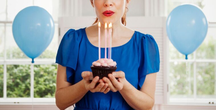 Woman holding cupcake with burning candles at home.