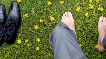 Shot of a man's feet in the grass. His black, dress shoes sit next to him.