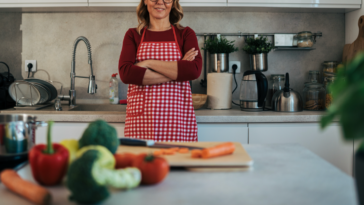 A woman wearing a red checkered apron with her arms crossed in a kitchen