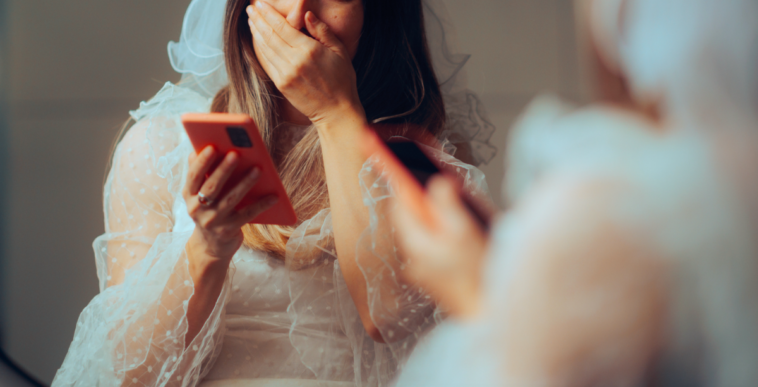 A bride looking at a smart phone and covering her mouth.