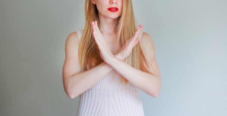 Photo of a pretty woman with her hands crossed as to show a 'no stop, forbidden' symbol on an isolated background.