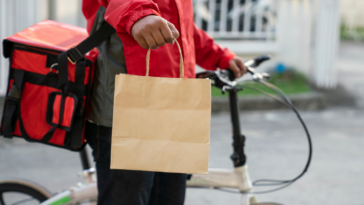 food in paper bag being delivered by person in red jacket on a bicycle
