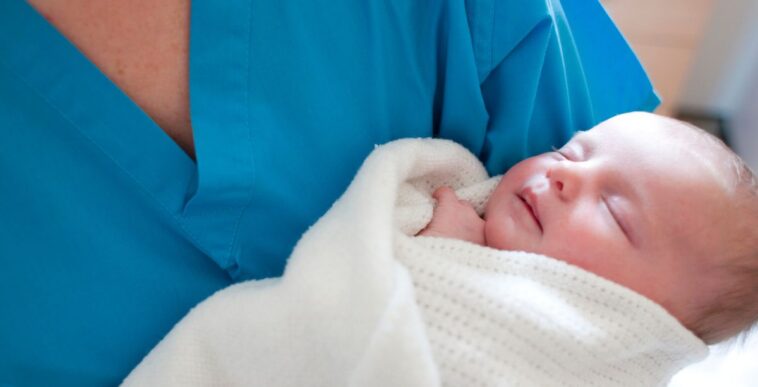 Newborn baby held by a nurse.