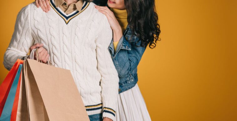 Cropped image of couple with shopping bags isolated on yellow background.