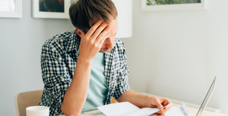 Pensive man thinking about high prices. Managing family finances. Rise of utilities, gas, electricity, rental charges, water bill due to inflation and global crisis. Facing downturn including energy. Planning family budget while sitting in kitchen.