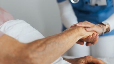 Close-up of caregiver holding senior client hand. Support from nurse to patient, taking care of elderly man in hospital. Emotional support and care in healthcare, hospice care.