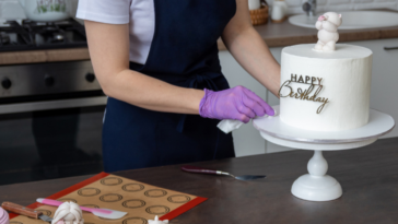 A woman decorating a cake with the words "Happy Birthday" on it.