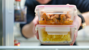 A man putting two tupperware containers full of leftovers in the fridge.