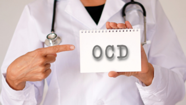 A person in a lab coat with a stethoscope around their shoulders holding a card that says OCD on it.