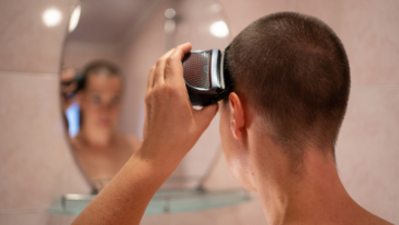 A woman looking into a mirror and shaving her head.
