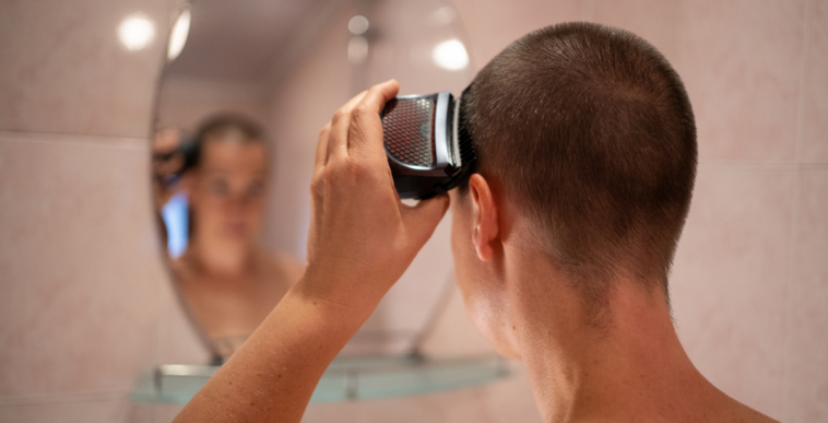 A woman looking into a mirror and shaving her head.