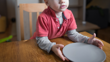 A little boy sitting at a table, holding an empty plate.