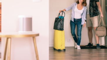 A couple entering a living room with luggage.