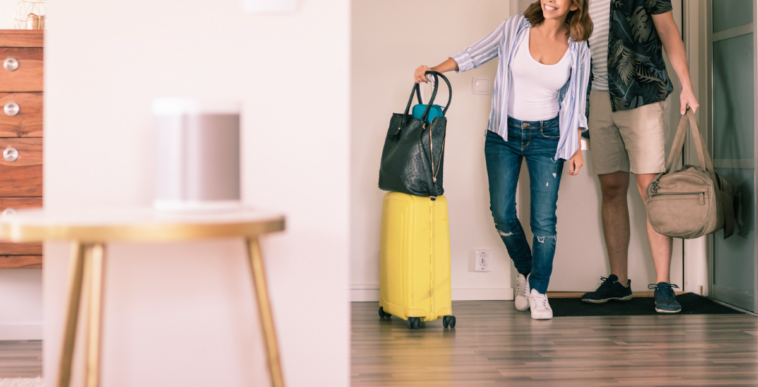 A couple entering a living room with luggage.