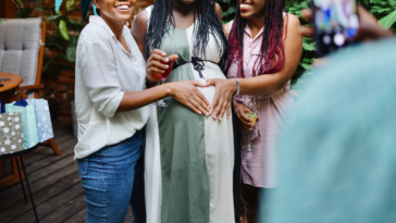 Two women putting their hands on a pregnant woman's baby bump.