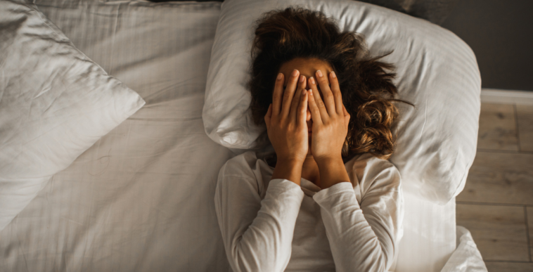 A woman lying in bed with her hands covering her eyes.