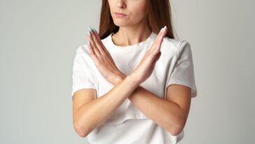 Young woman showing you crossed hands sign declining your request on gray background studio shot.