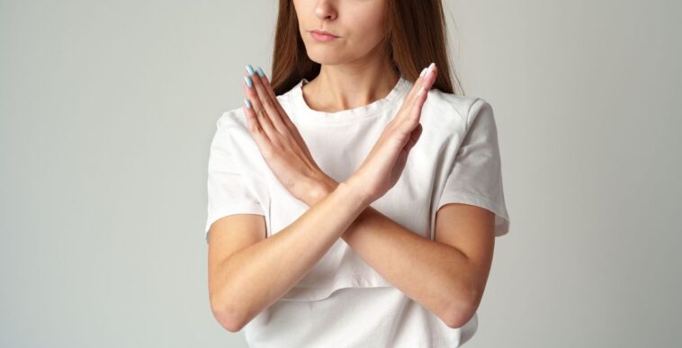 Young woman showing you crossed hands sign declining your request on gray background studio shot.