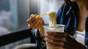 A woman is enjoying eating instant noodles in her living room at home.