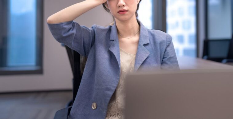 Stressed young businesswoman in the office, holding her hand to her head.