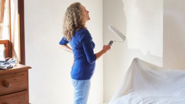 A mature woman painting her bedroom white.