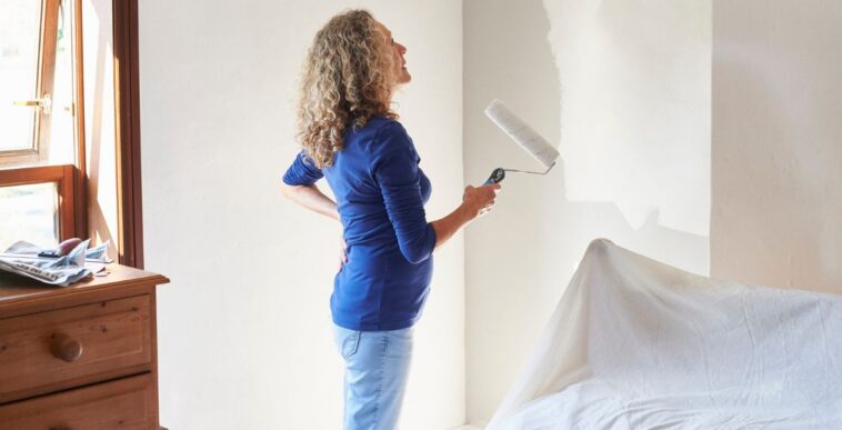 A mature woman painting her bedroom white.