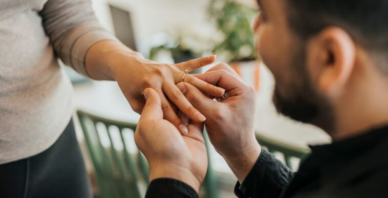 Romantic man putting ring on girlfriend's finger at home.