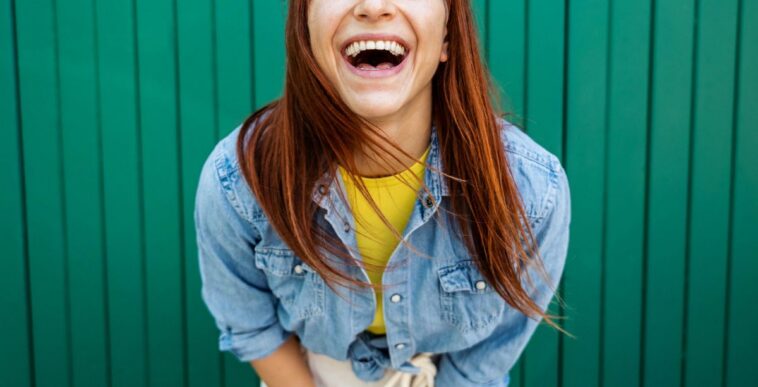 Young, beautiful red hair woman laughing at the camera - Portrait green background.