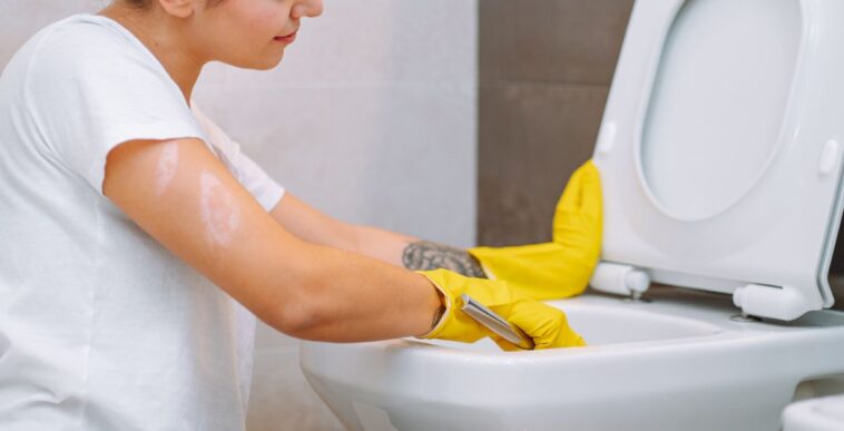 A young girl wearing yellow household gloves cleans the toilet bowl. House cleanliness, cleaning service.