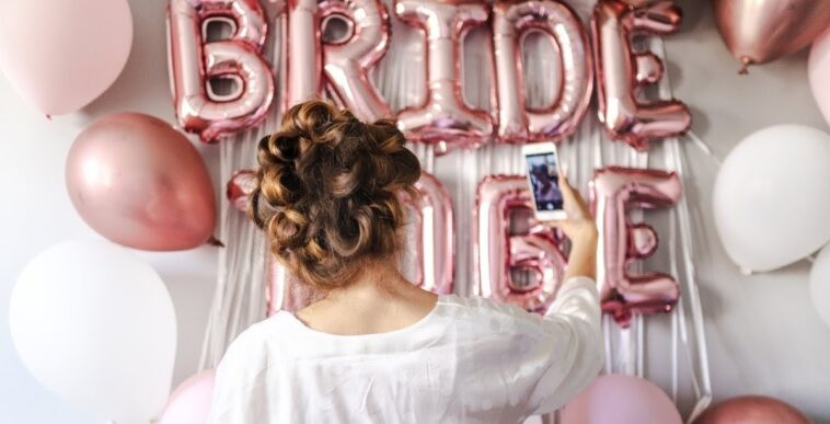 woman in white takes selfie in front of bridal shower decorations