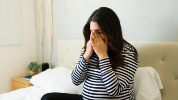 crying pregnant woman seated on bed