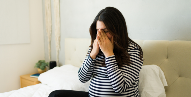 crying pregnant woman seated on bed