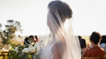 Side view of a young bride wearing a veil, standing with a flower bouquet at a wedding ceremony.